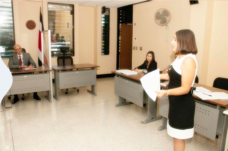 tres personas en una audiencia, una de ellas de pie con un papel en la mano